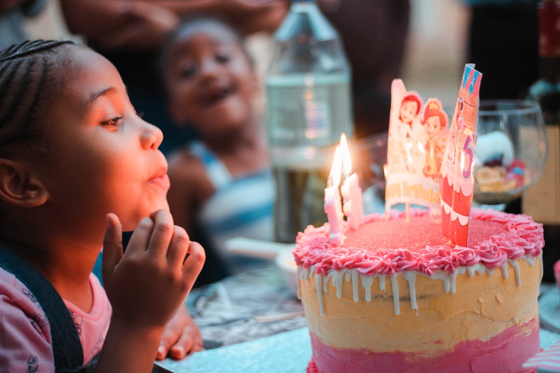 Child blowing out birthday candles while friends watch