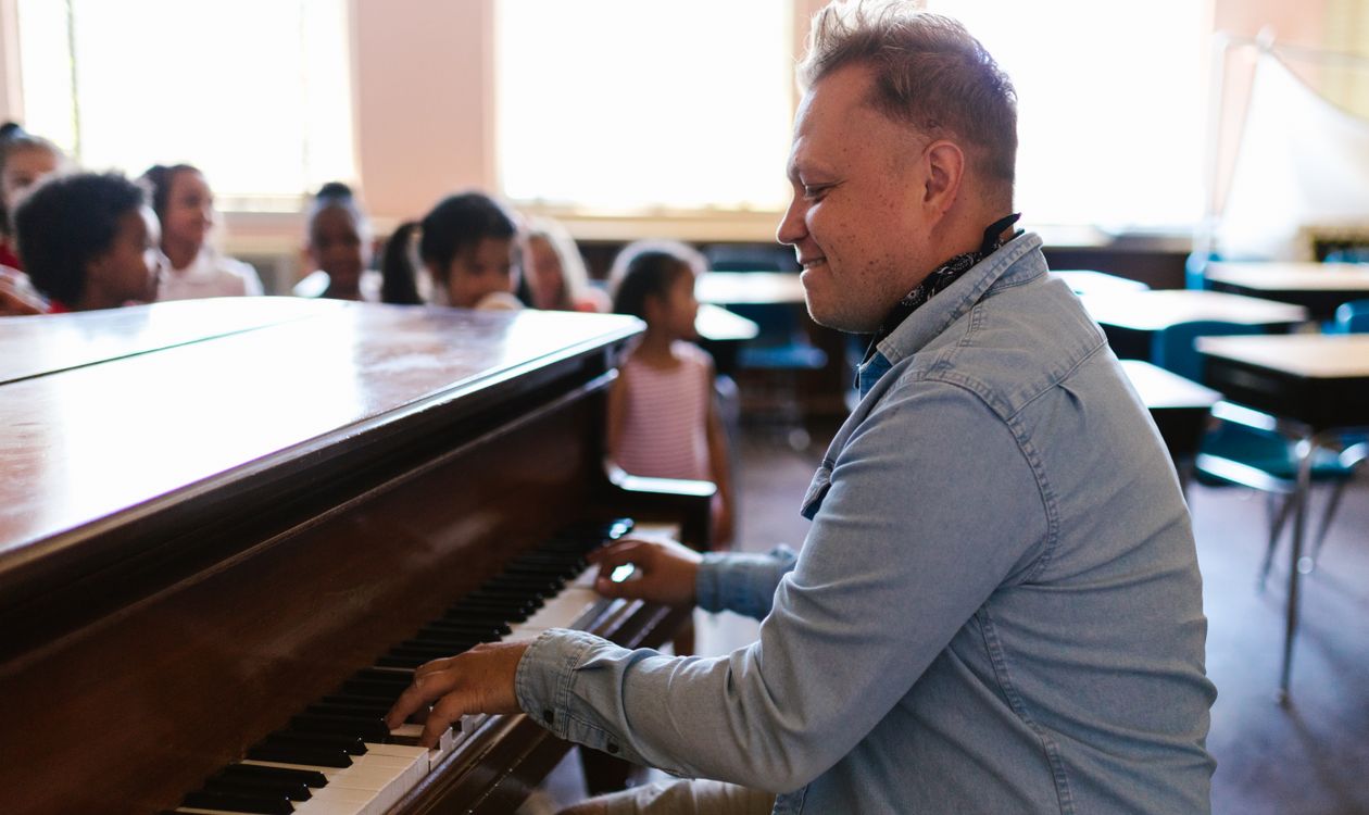 A teacher plays the piano for a group of children in a classroom