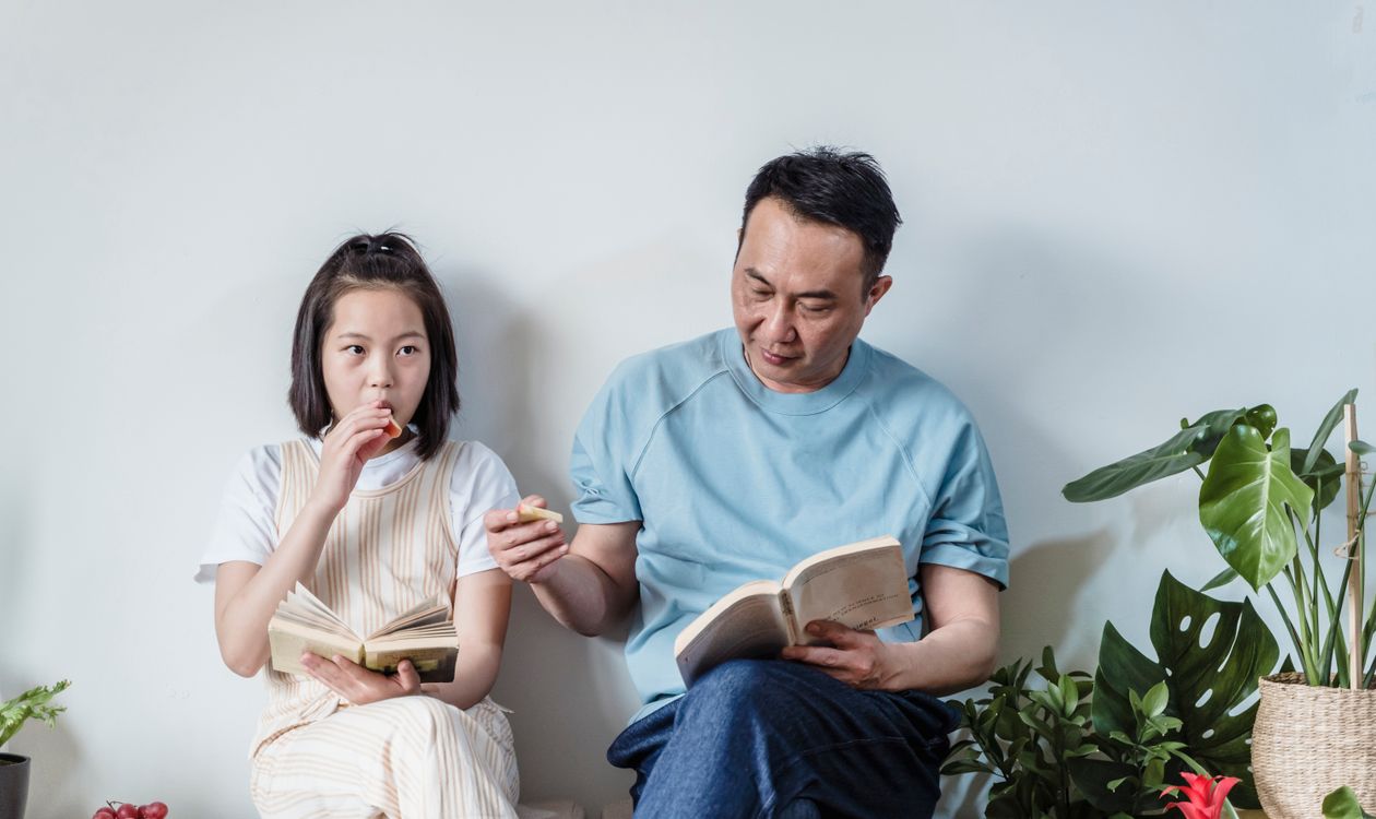 A father and daughter read side by side on a sofa