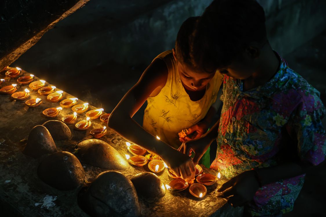 Children lighting rows of diyas on the ground at night