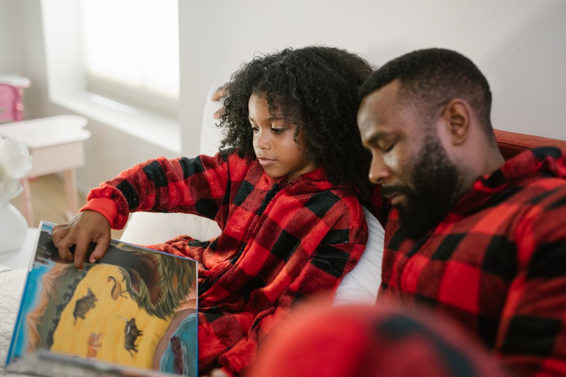 A father reading a book with his young daughter at home