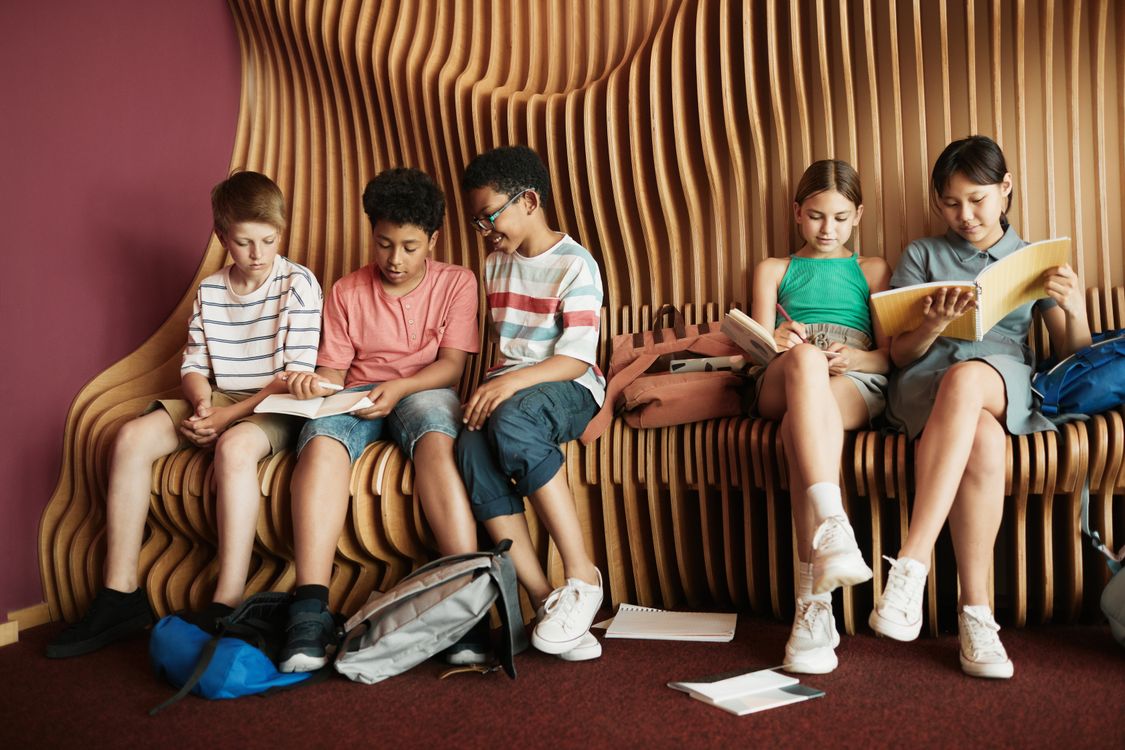 A diverse group of children reading a book together on a bench