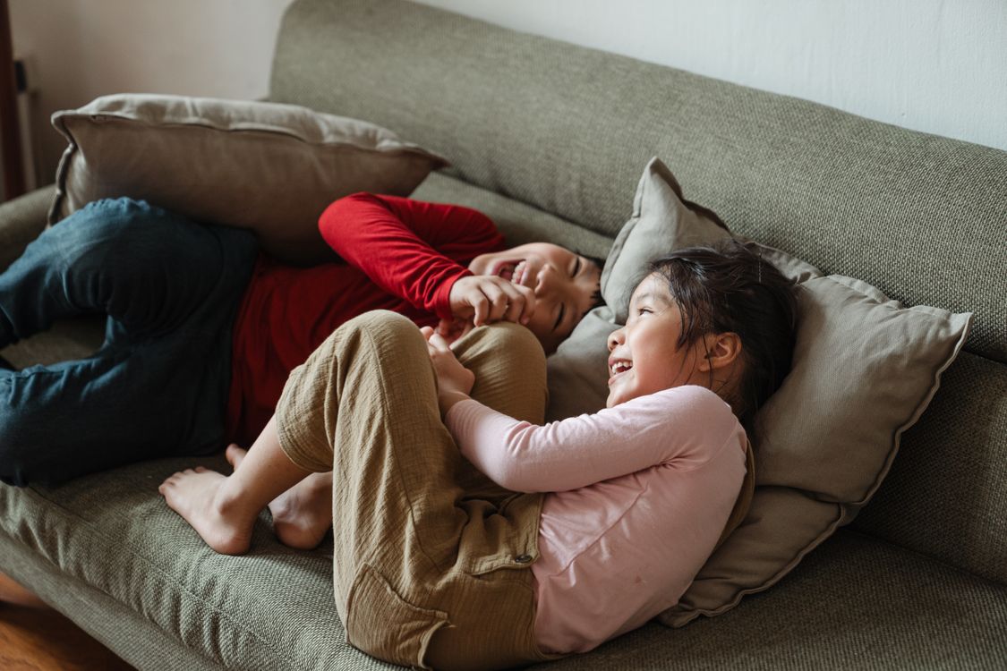 Two children playing together and laughing on a sofa
