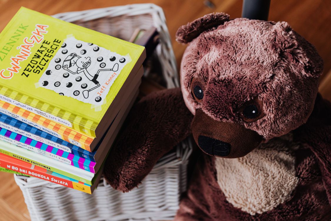 Stack of colourful picture books beside a teddy bear in a child's room