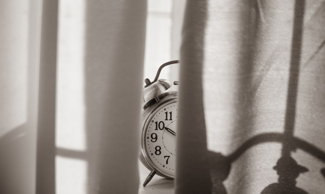 An alarm clock on a windowsill, half hidden behind the curtain