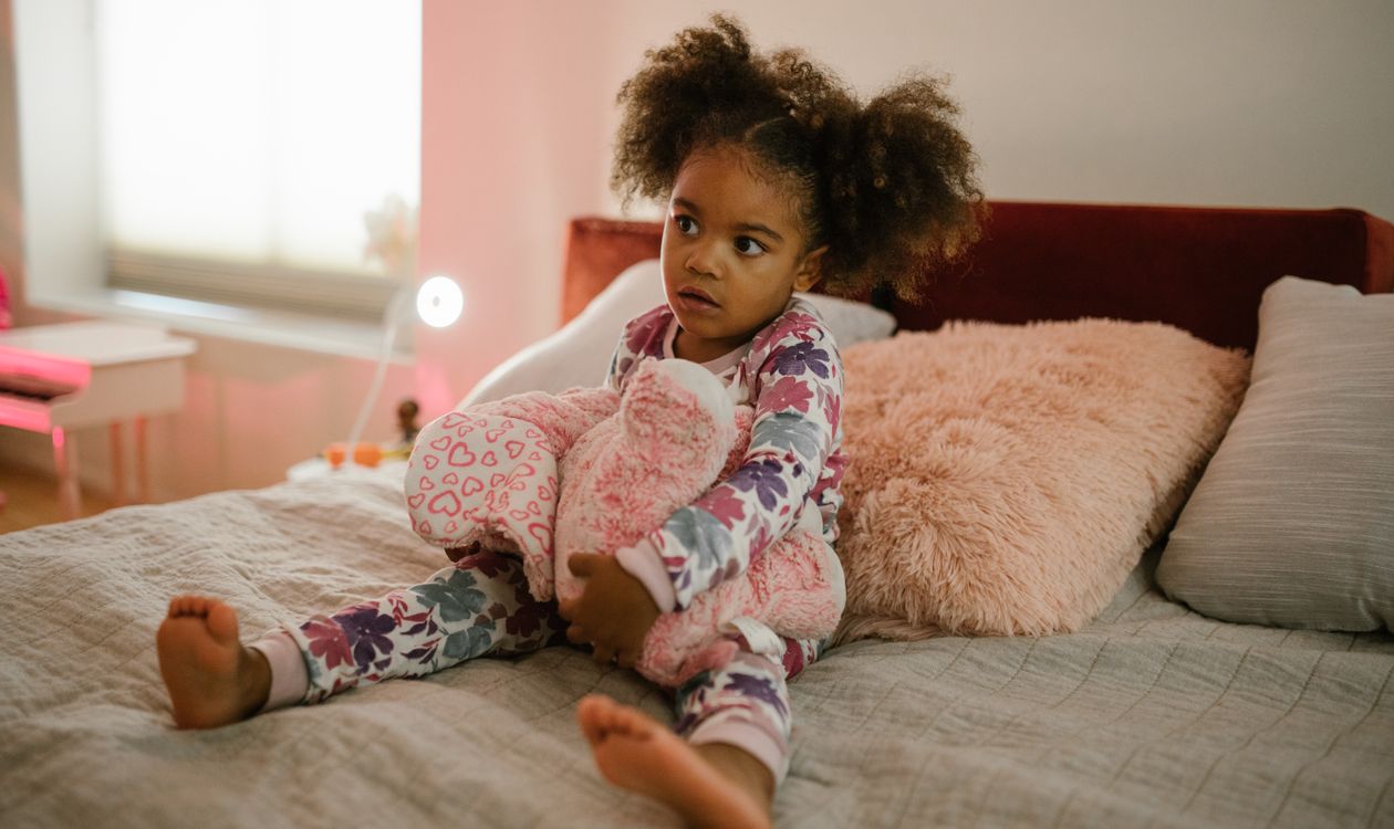 A girl in pyjamas sitting awake on her bed with her soft toy
