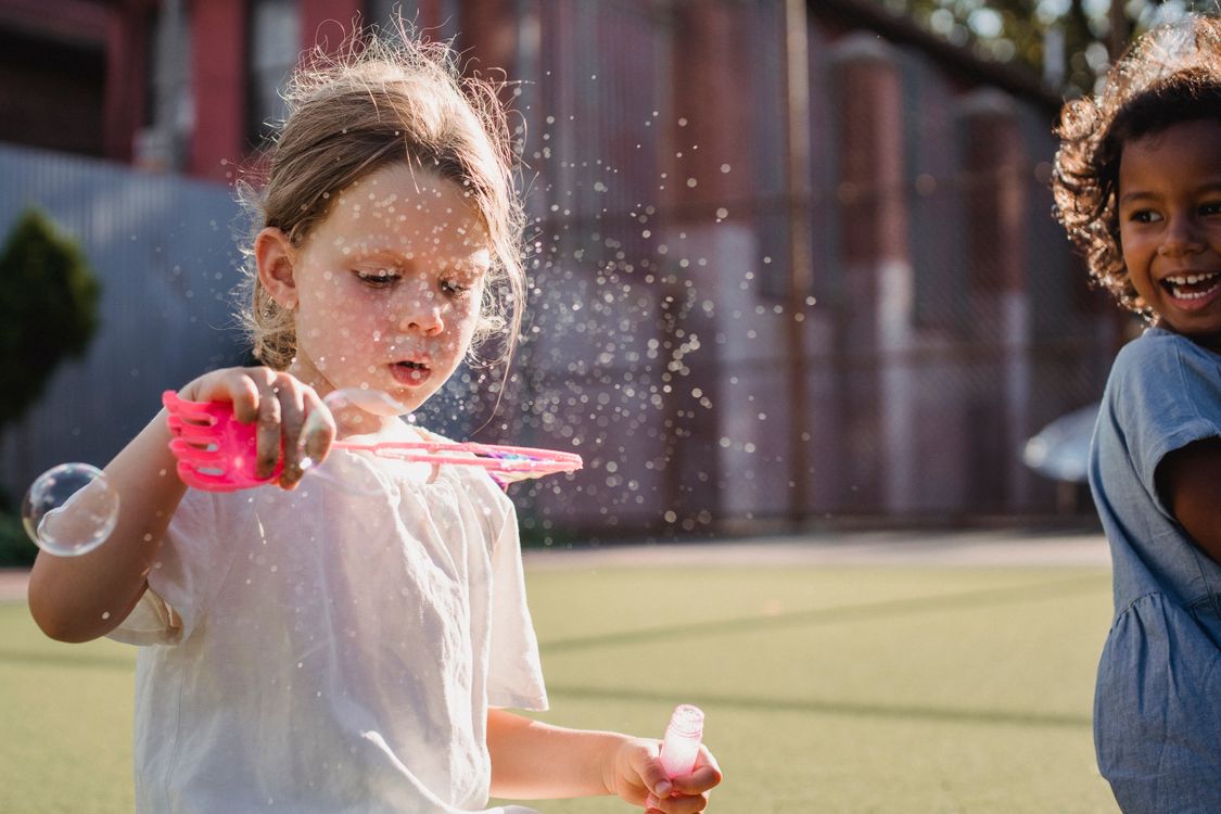 Two children blowing bubbles outdoors in the sunshine